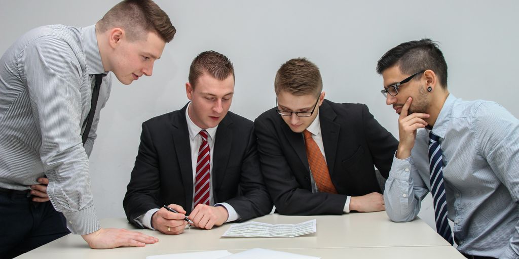 four men looking to the paper on table